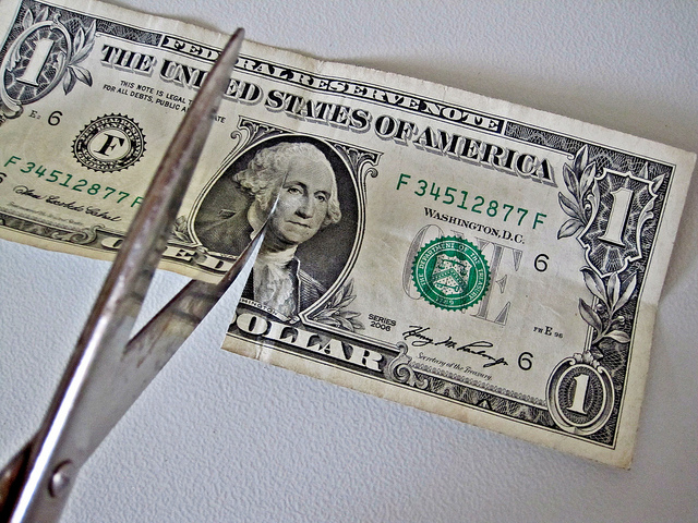 scissors cutting one dollar bill in half